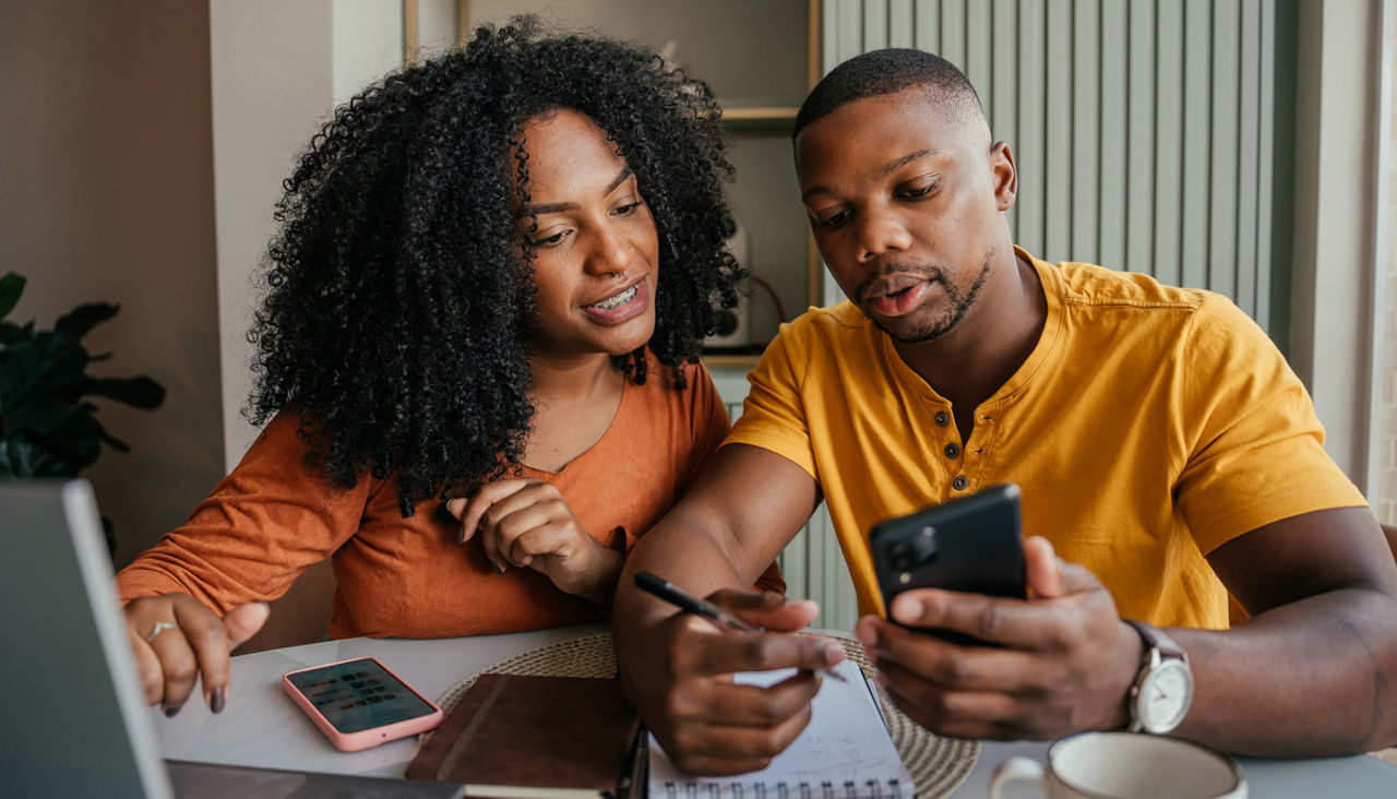 Couple looking at a smartphone while writing 