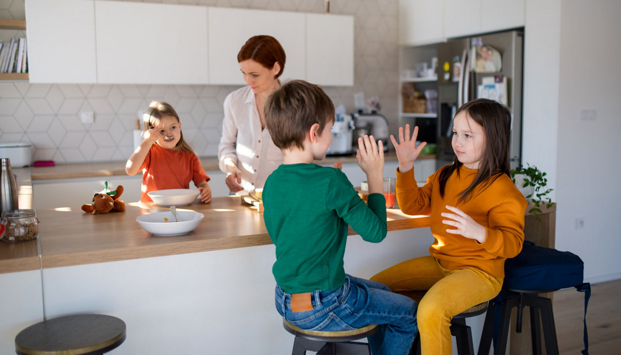 Mother preparing breakfast in kitchen at home with her three young children sitting at counter