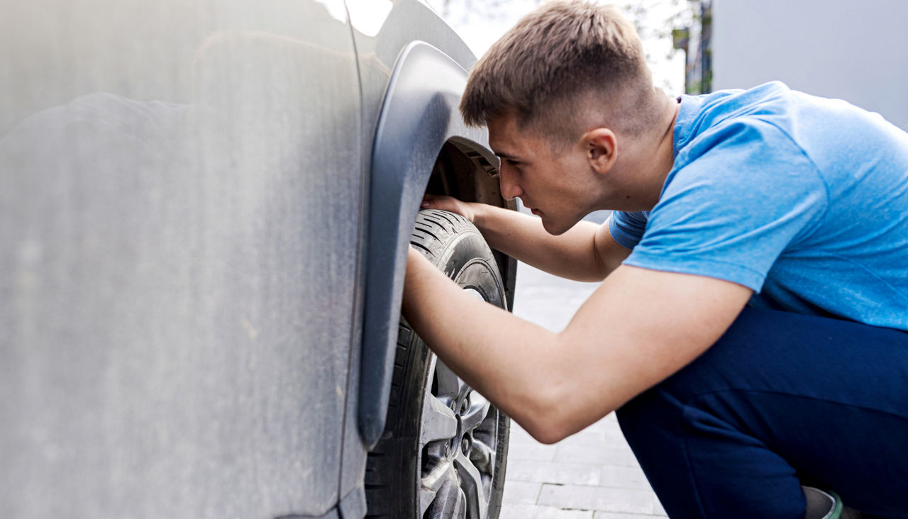 man checking his tire on his car