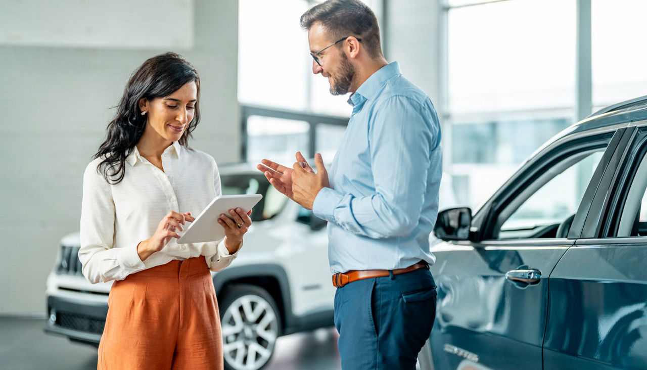 Cheerful car dealership customer talking to auto sales consultant