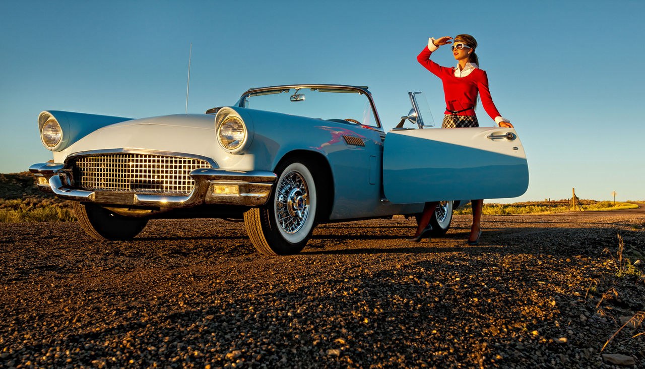Woman standing behind open door of powder blue 1957 Ford Thunderbird convertible