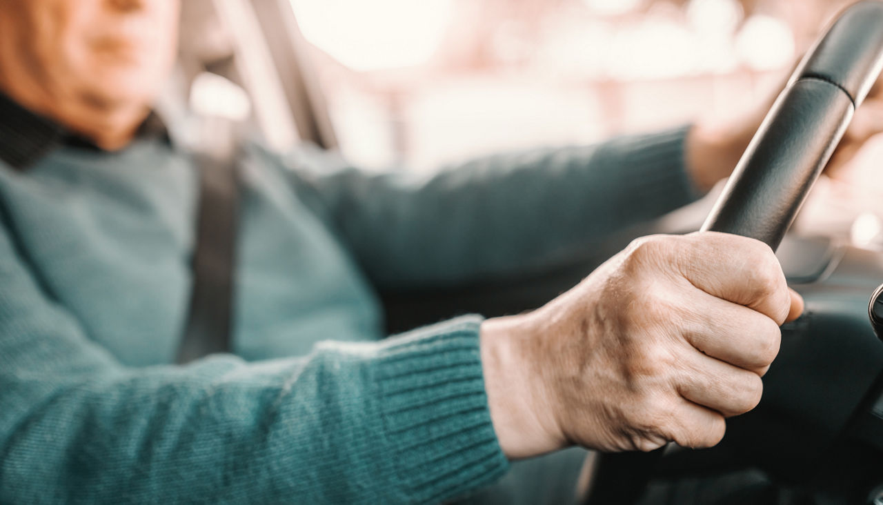 Close up of senior man holding hands on steering while and driving his car.