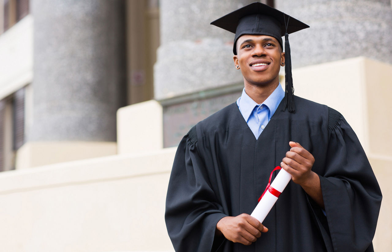 Young graduate in cap and gown holding his diploma