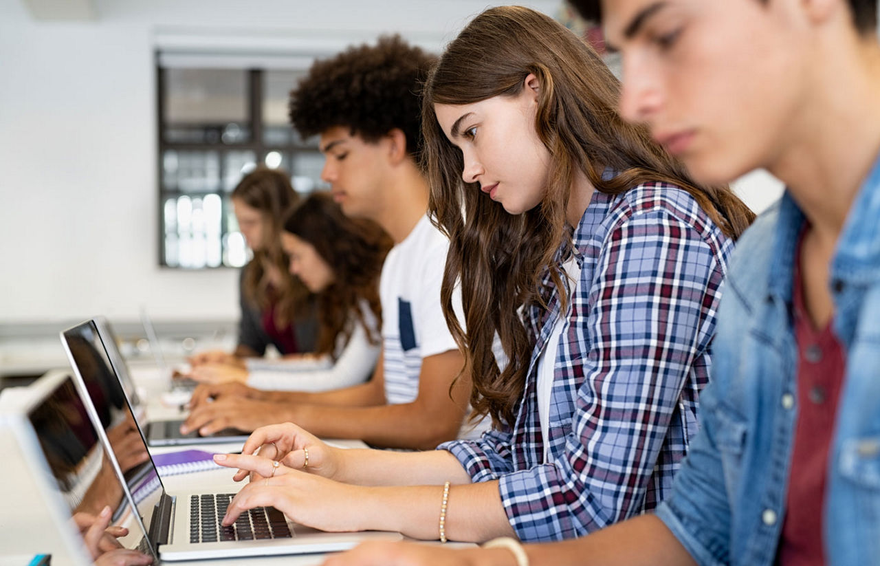 Group of high school students using laptop in classroom