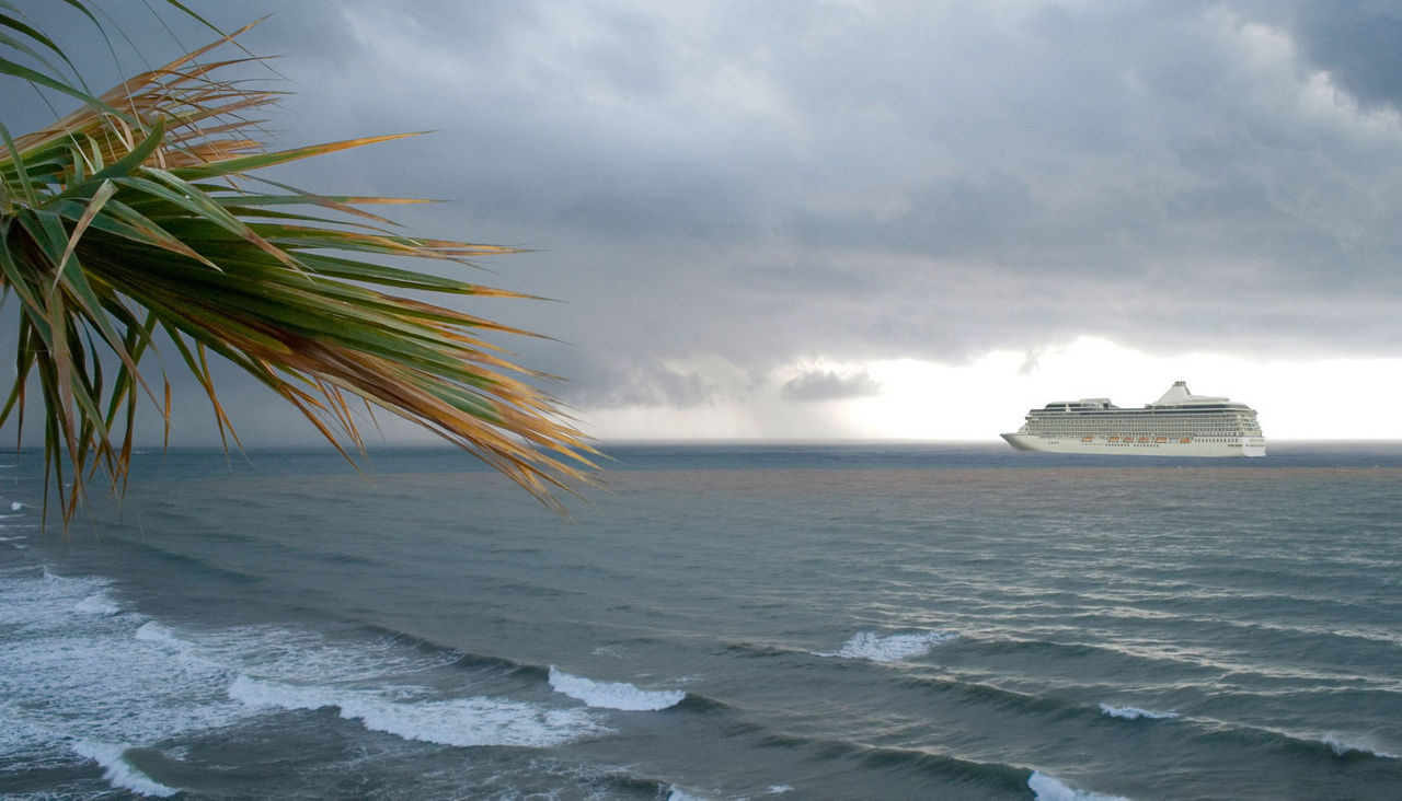 Massive cruise ship navigates the ocean by a beach on a cloudy day