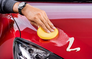 A male hand waxing a bright red car's hood.