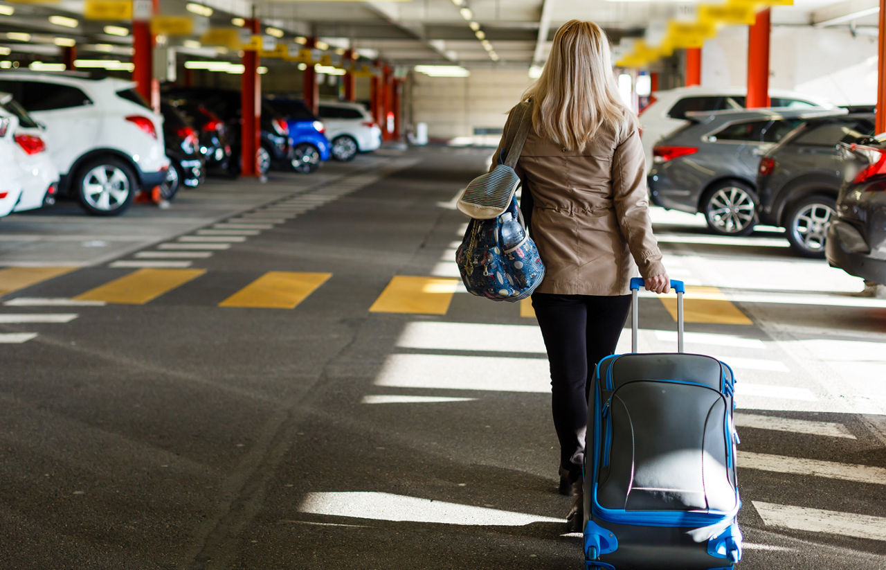 Woman with a suitcase walking through an airport parking garage. 