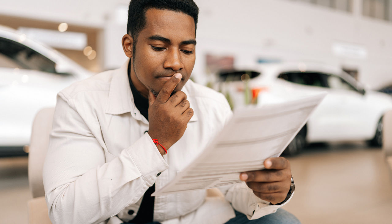 Portrait of serious pensive black male buyer carefully reading car purchase agreement before signing in dealership office.