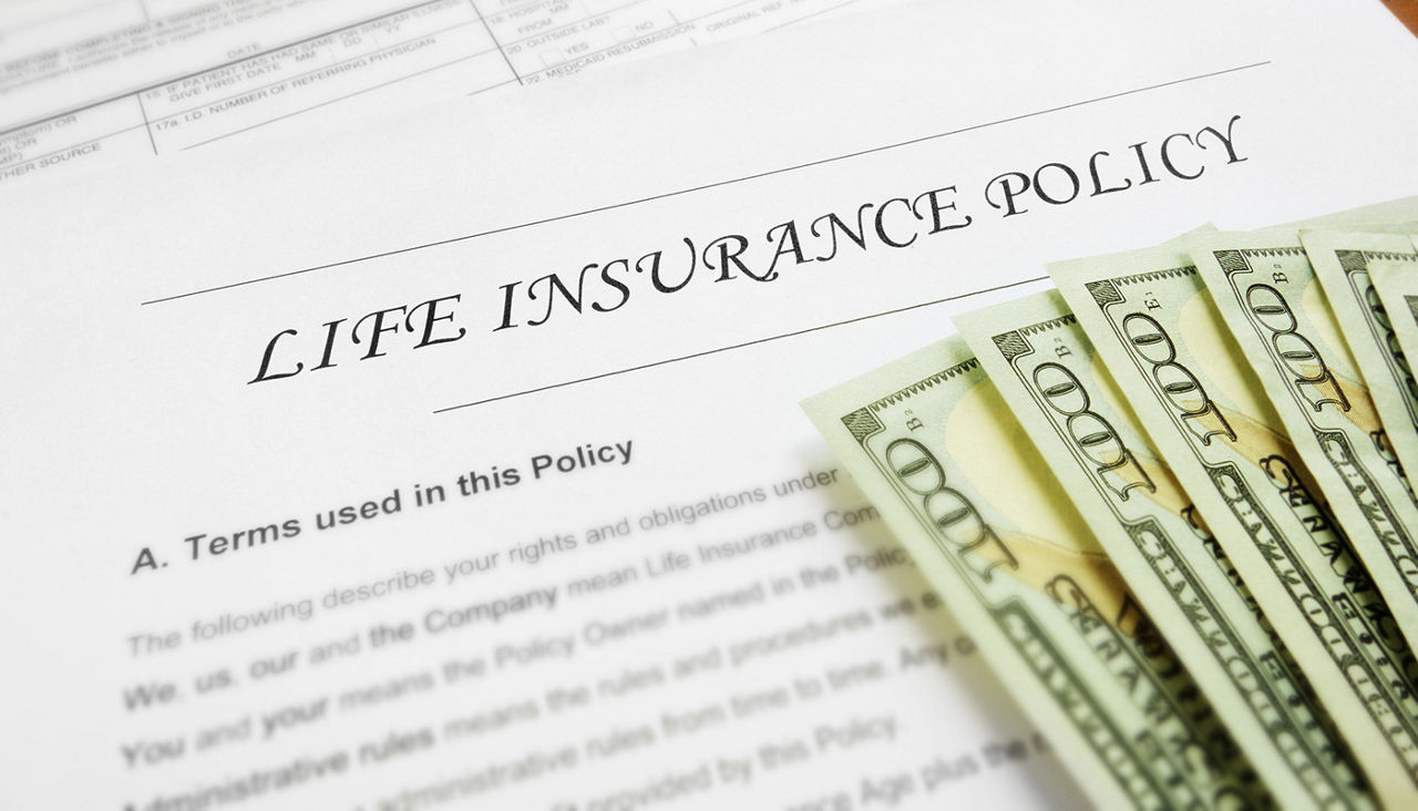 Life insurance policy paper with hundred dollar bills on top