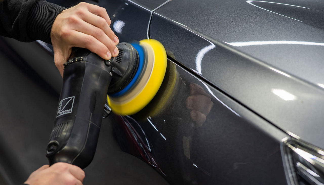 A mechanic polishes the surface of a car body.