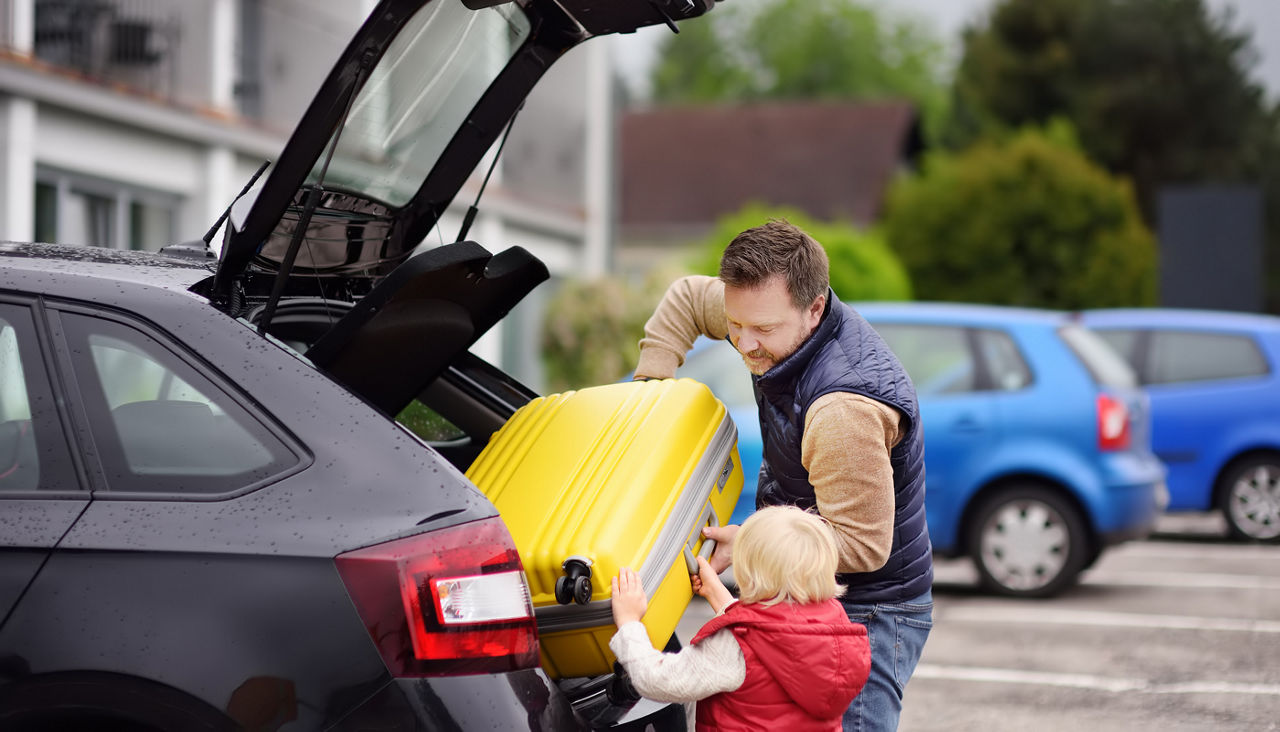 Handsome man and his little son going to vacations, loading their suitcase in car trunk