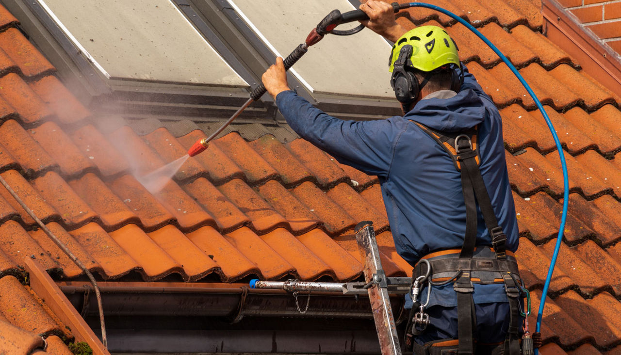 Man washing tile roof with pressurized water