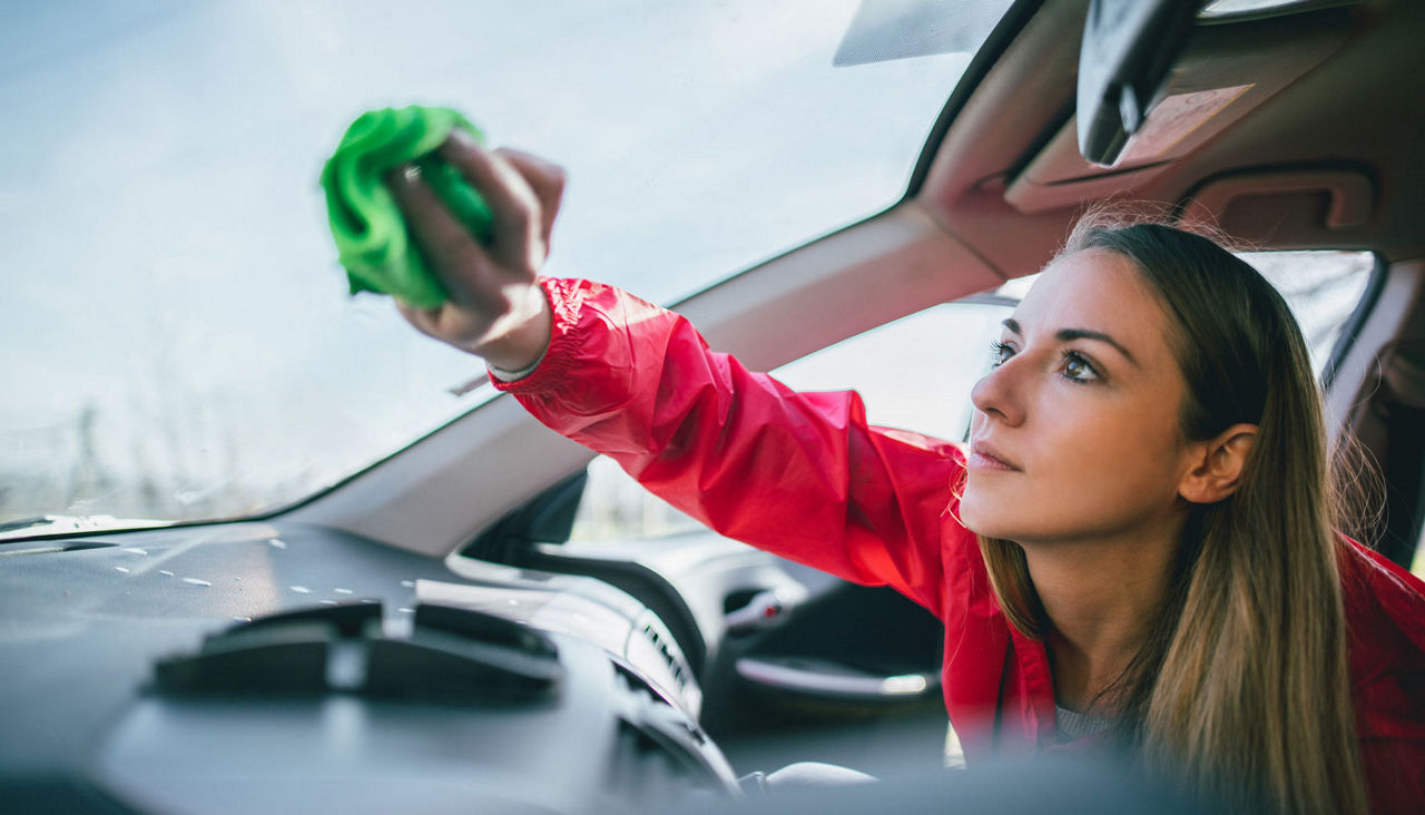 Woman cleaning inside of car windshield.