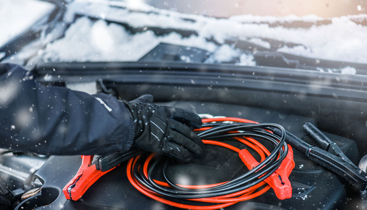 Hands grabbing jumper cables from a car in wintery snow