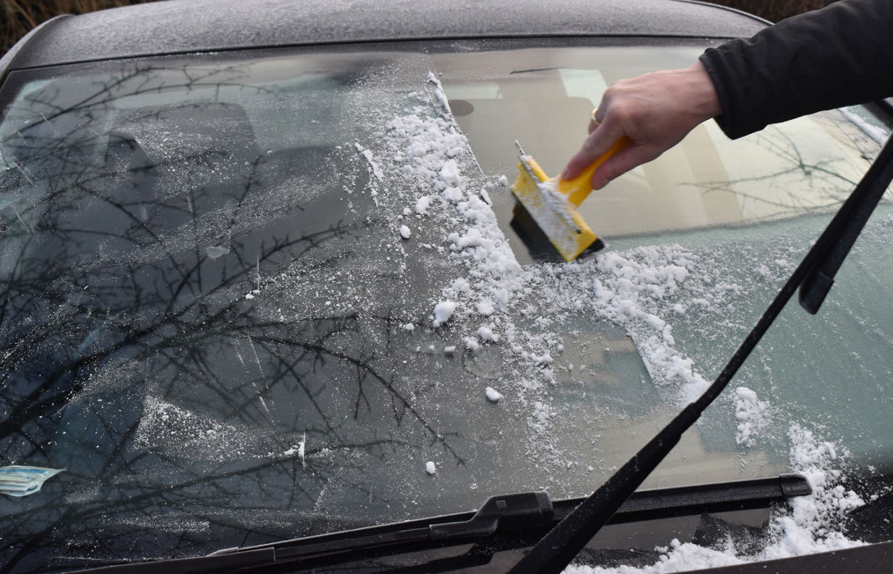 Frosty morning, ice cover window car, bad weather conditions, scraping ice from the car windows by hand with an ice scraper early in the morning