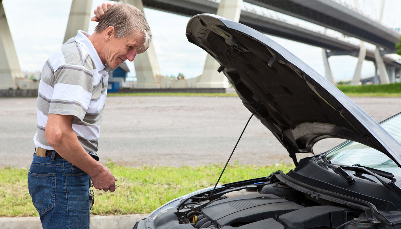 Confused mature driver standing in front of vehicle with opened engine compartment hood