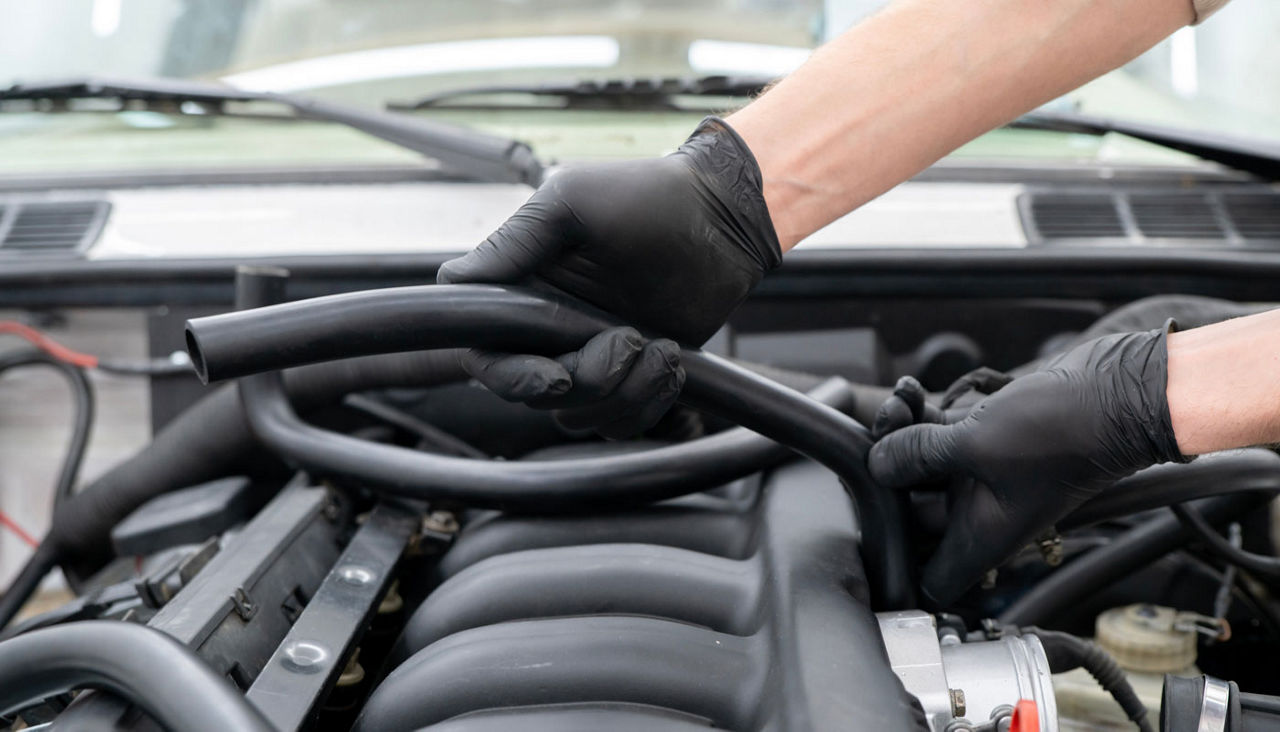 Mechanic works on installing air hose inside the engine compartment of a vehicle