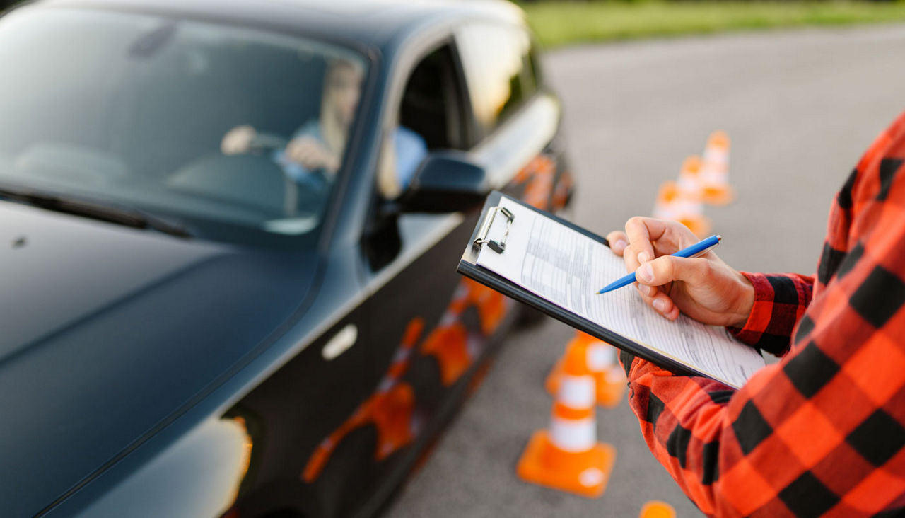 Instructor with checklist and teen in car taking exam