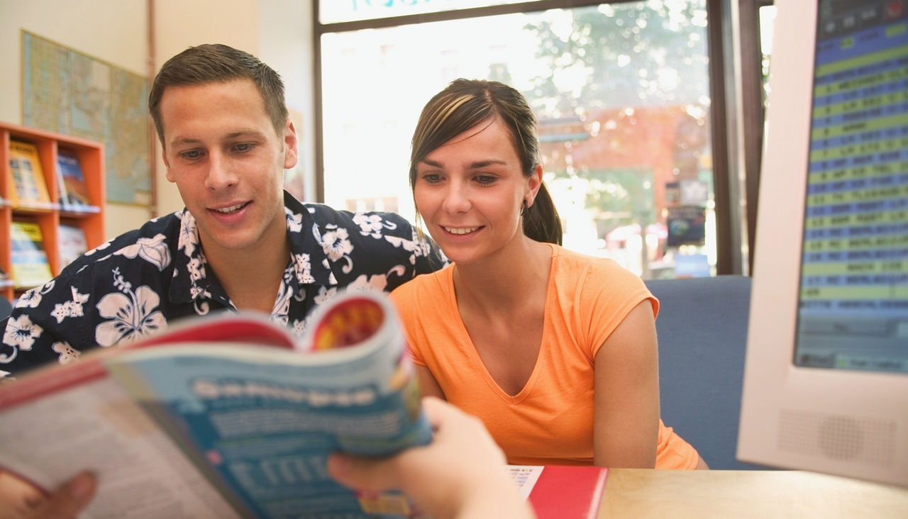 Young couple looking at brochure shown by travel agent