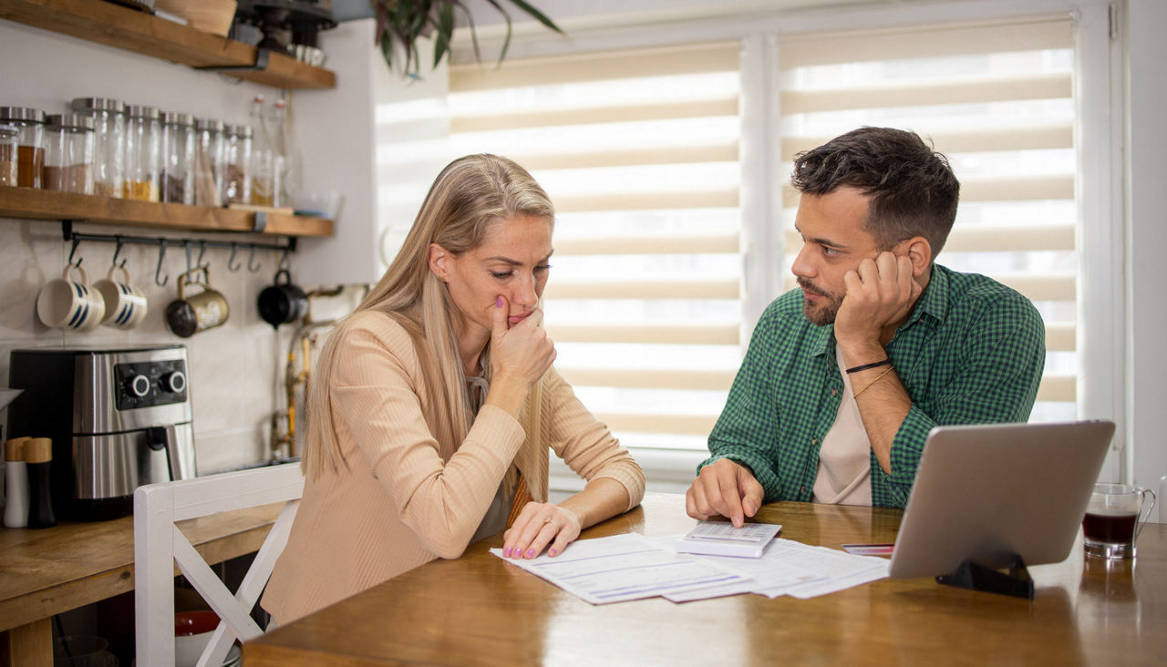 Young couple sitting at kitchen table with paperwork and a laptop