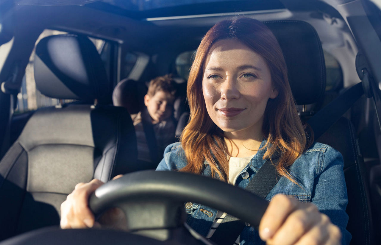 Woman driving car with child in backseat on a sunny day