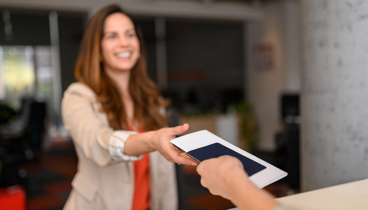 Businesswoman giving passport and documents to smiling female airline check in attendant at airport