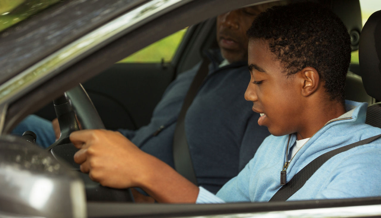 Teenage boy in driver's seat of car, learning how to drive with his father beside him