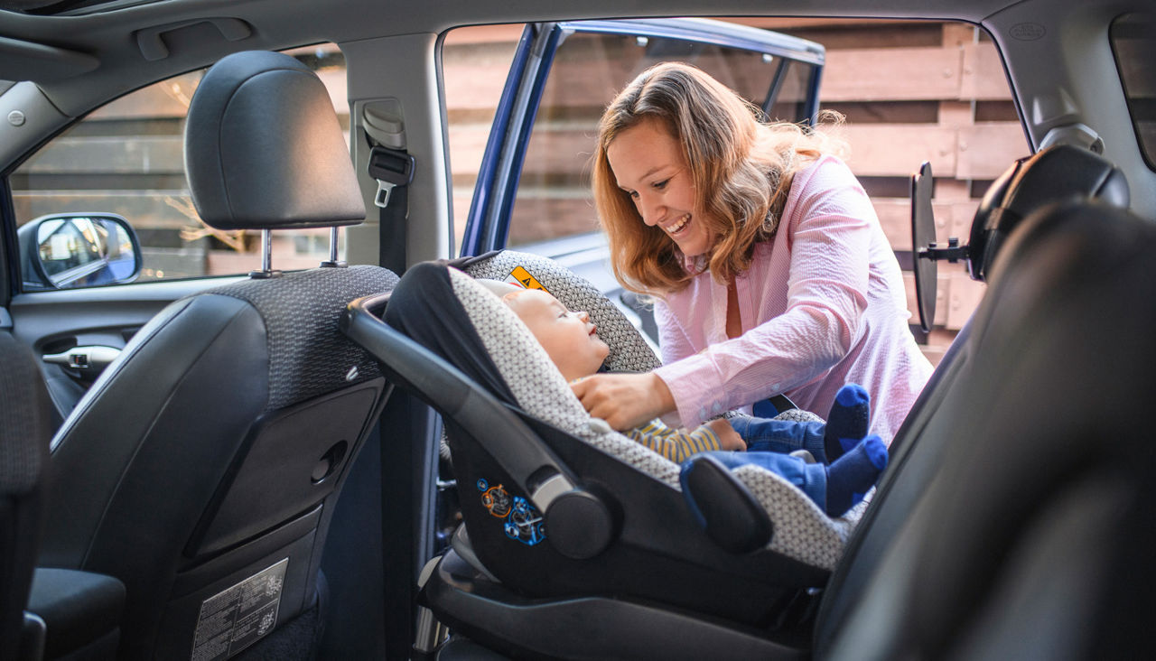 Mother putting baby in rear-facing car seat in vehicle