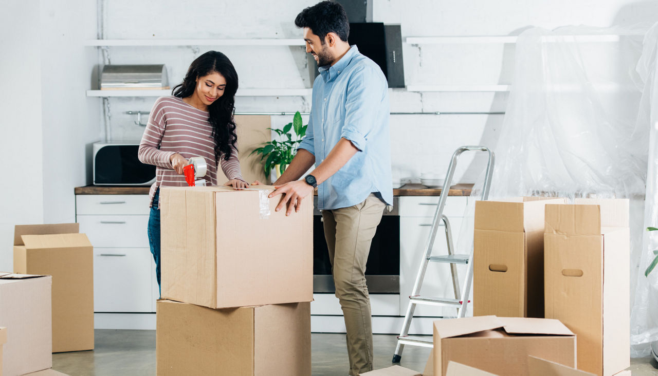 cheerful latin couple packing boxes while moving to new home