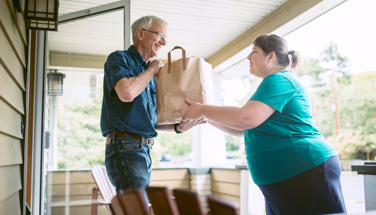 A kind and caring neighbor or friend delivers fresh produce from the grocery store to an elderly man at his home