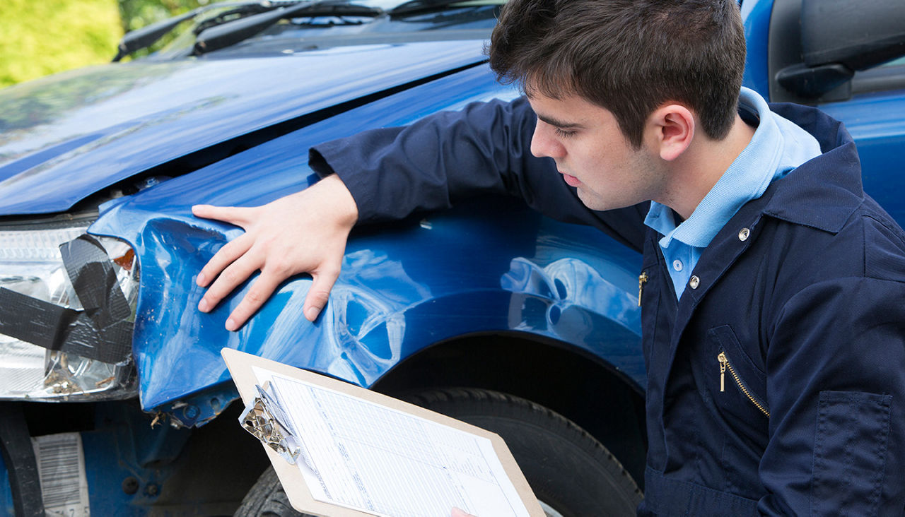 Man with clipboard assessing damage to wrecked car