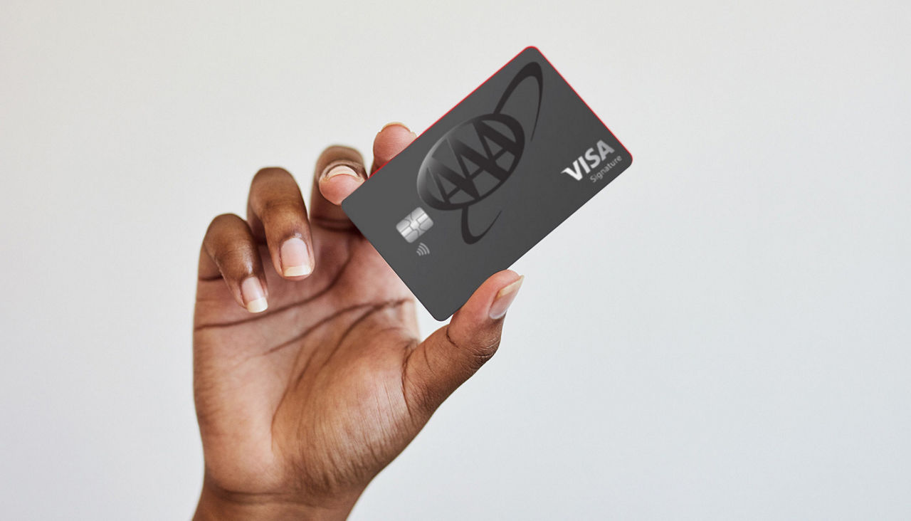 A hand holds up the AAA Cashback Visa Signature Card