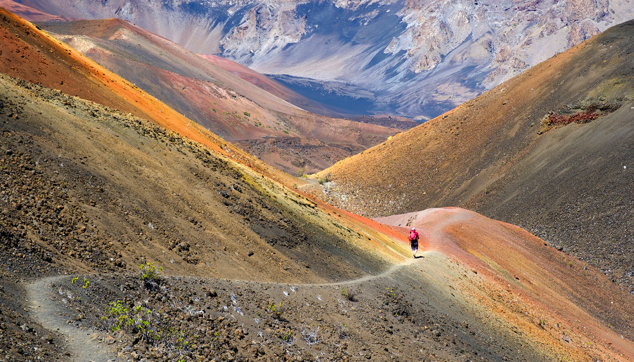 A hiker walks down the trail, surrounded by the vibrant colors within the Haleakala Crater on Maui.