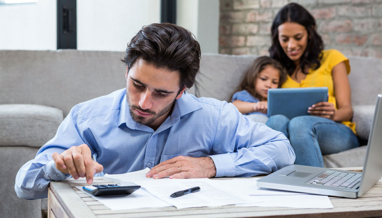 Husband paying bills in living room while wife is with child on couch