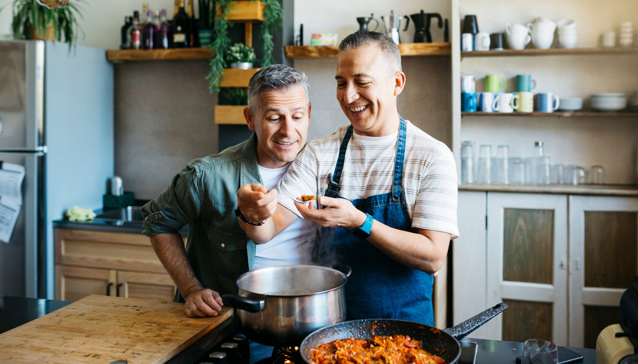 Mid adult cheerful gay couple talking and having fun while cooking in a kitchen