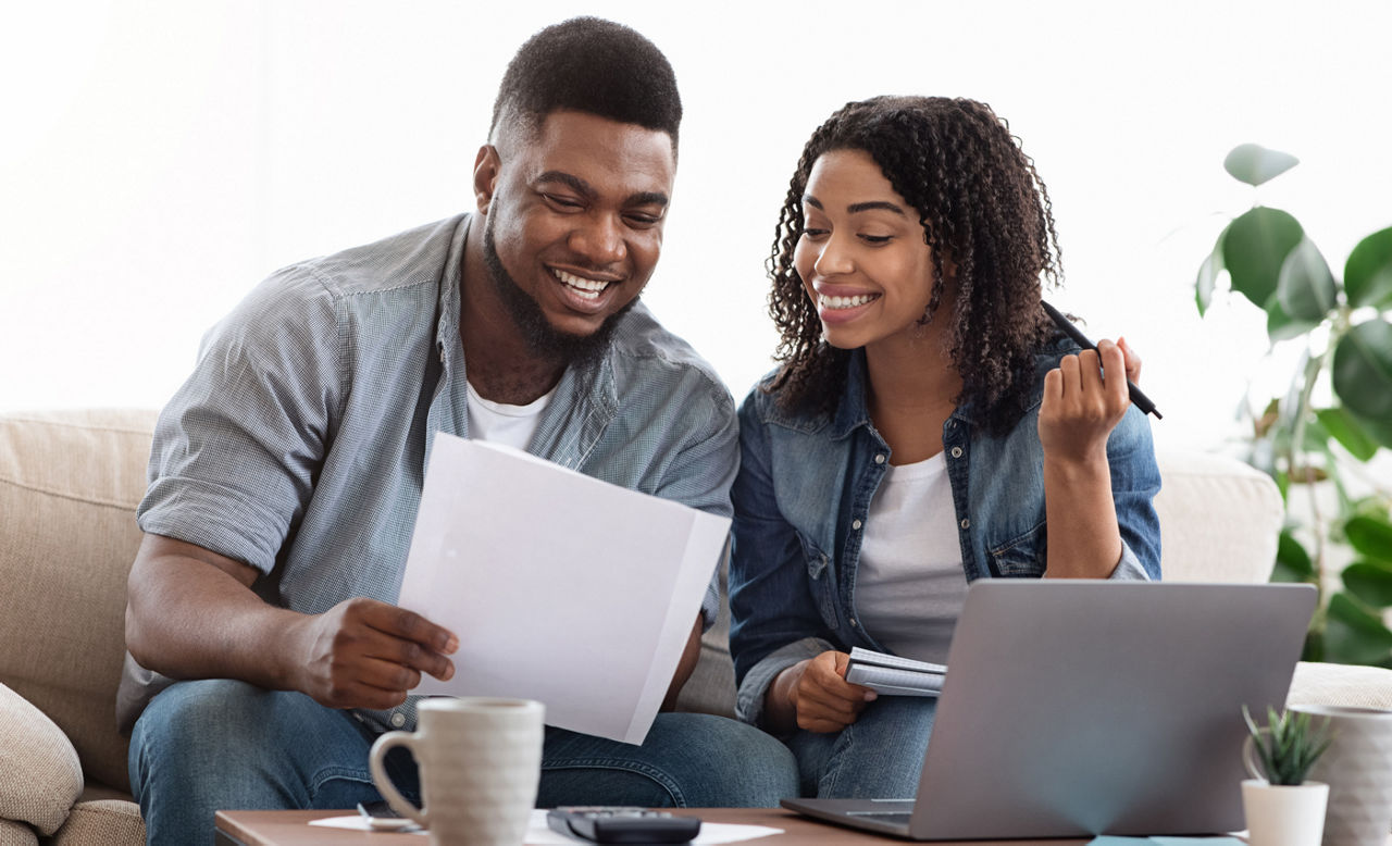 Couple smiling as they read financial documentation at home while planning family budget