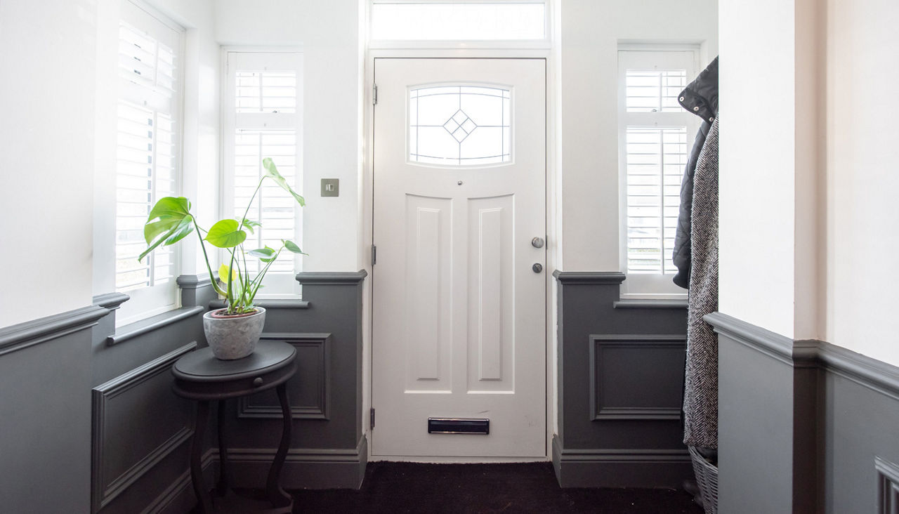 A general interior view of a hallway with white front door, windows with shutters