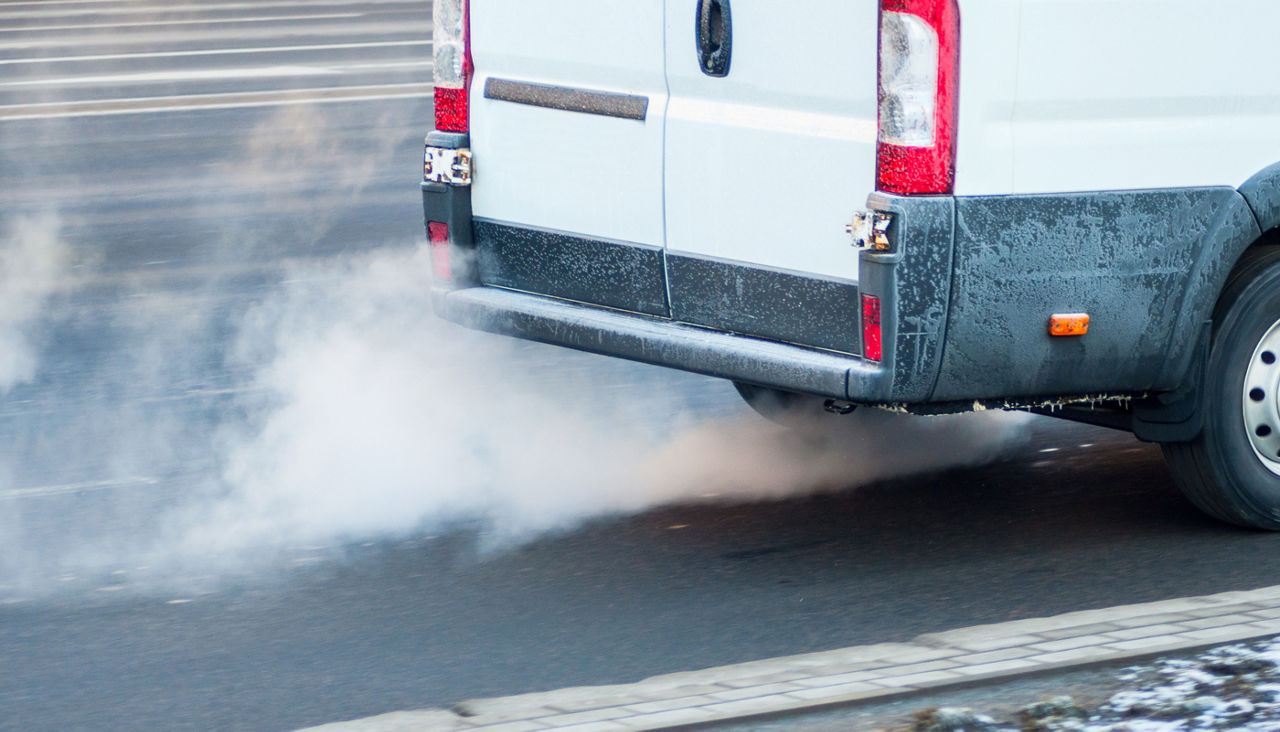 Pollution of the atmosphere by gas from the exhaust pipe of a white van in motion in the city