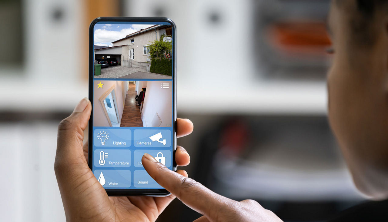 Woman holds smart phone displaying images of home interior and exterior above control buttons