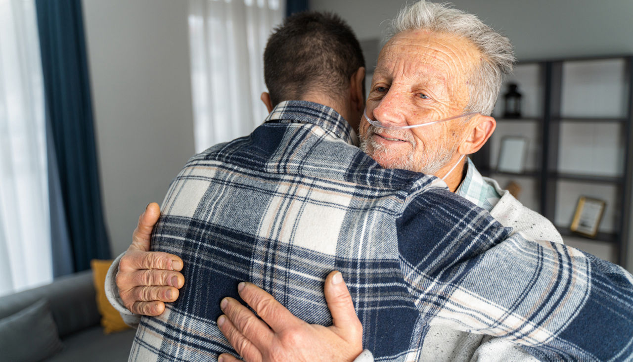 Young man hugs his senior father, who has an oxygen tube in his nose