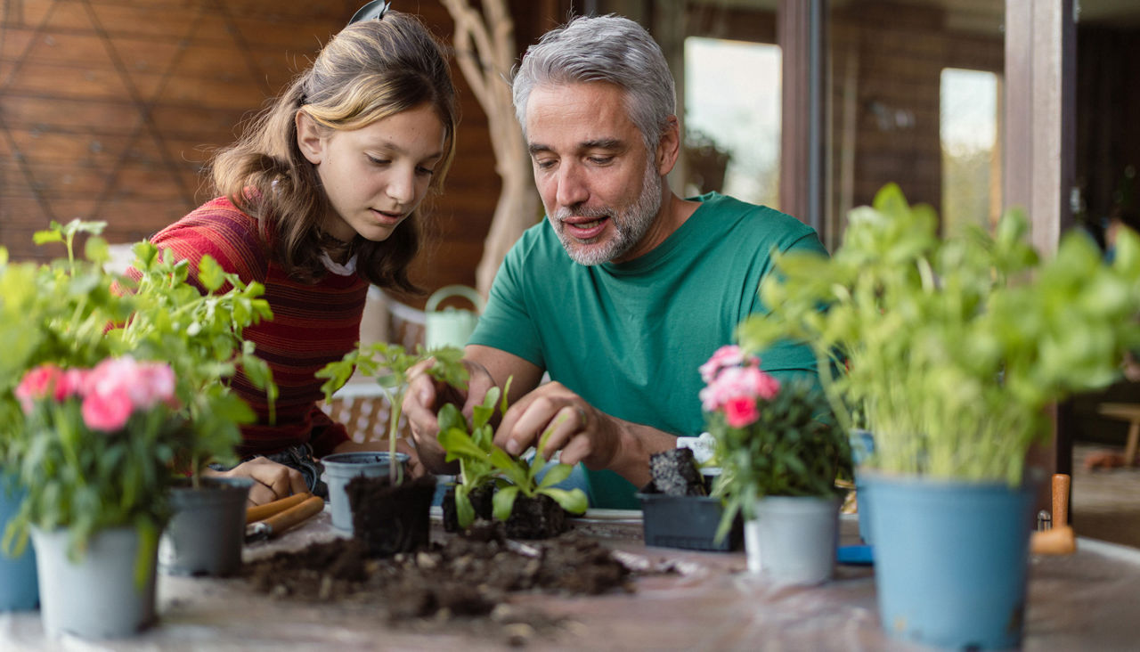 Teenage daughter helping father to plant flowers, home gardening concept