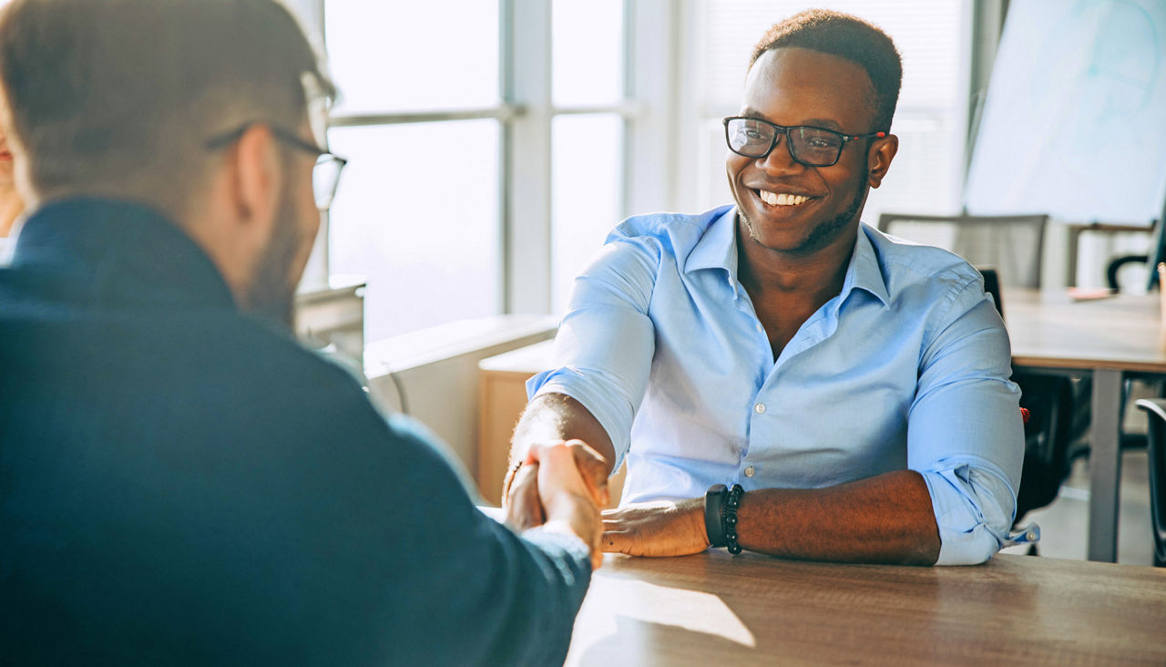 Two smiling men shaking hands across a table