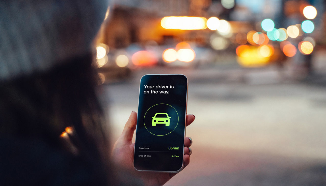 Over the shoulder view of young woman using mobile app on smart phone to arrange ride share on the street