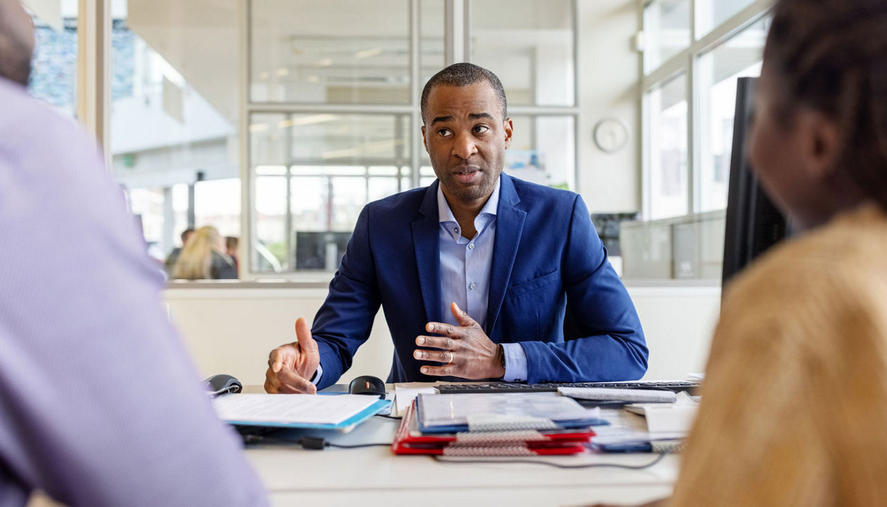Car showroom manager explaining the contract to buyer couple sitting in office