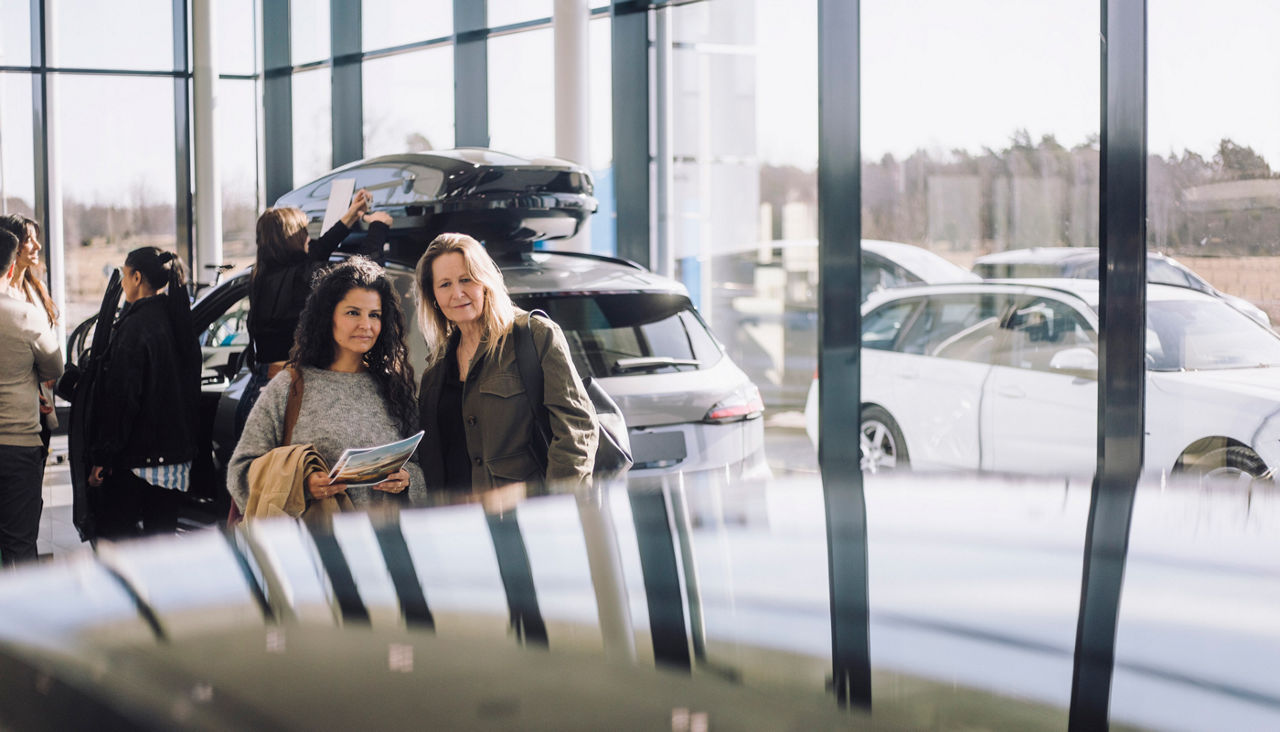 Two women holding brochure while looking at new car in showroom