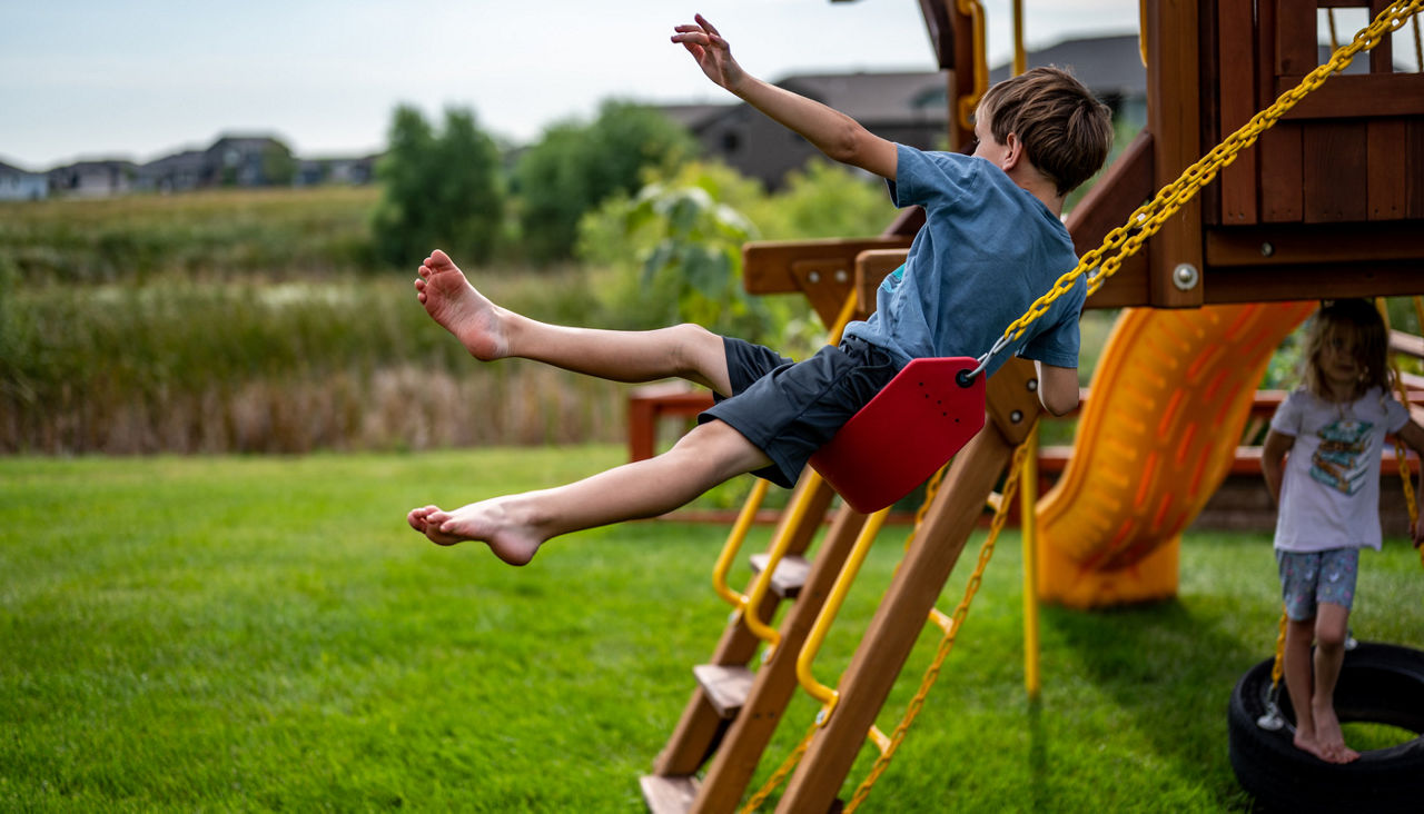Young boy jumping from a swing in his backyard as his younger sister watches