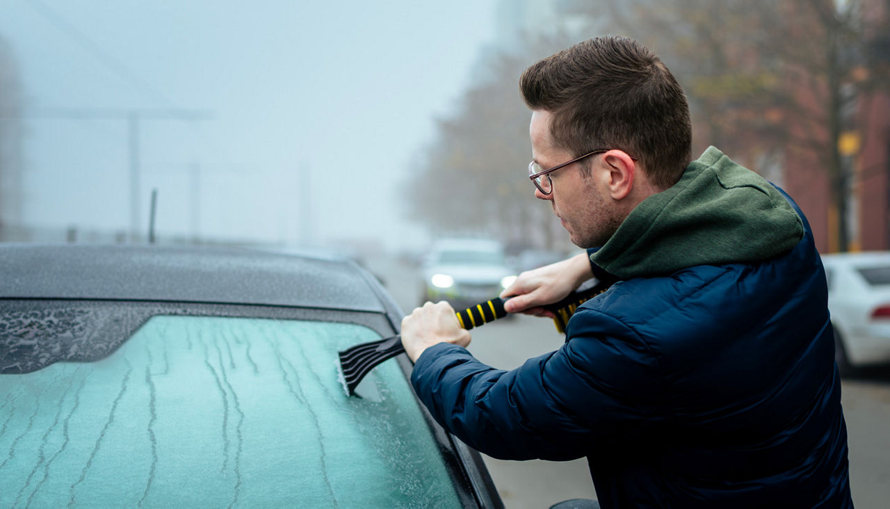Man scraping snow off car windshield
