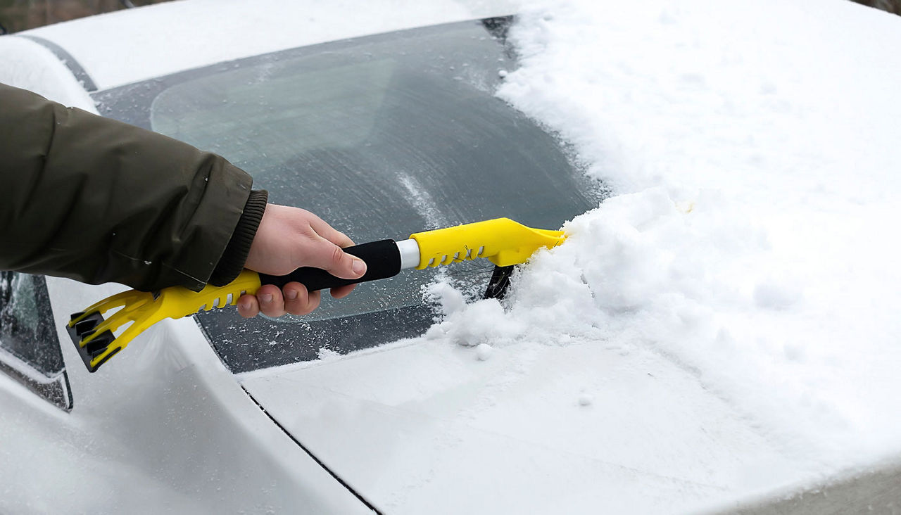 Person cleaning fresh snow after snowstorm from car in the winter