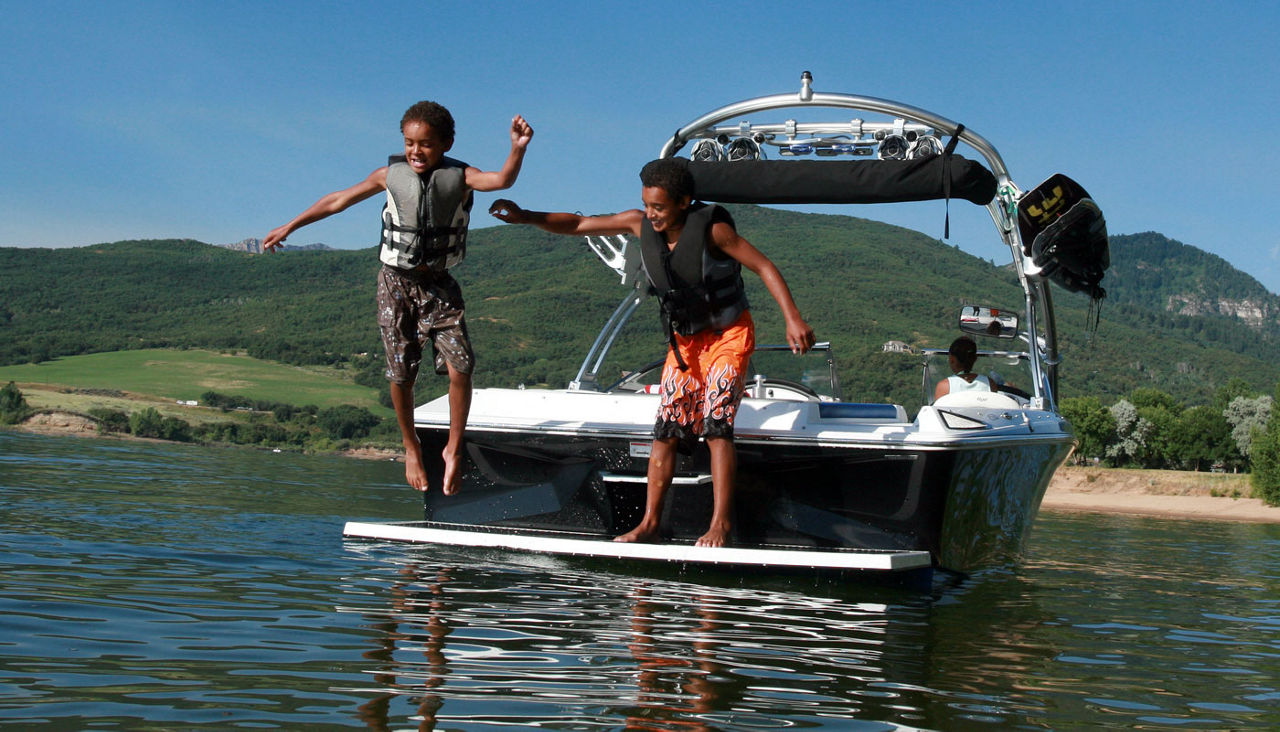 kids jumping from back of a boat in a lake