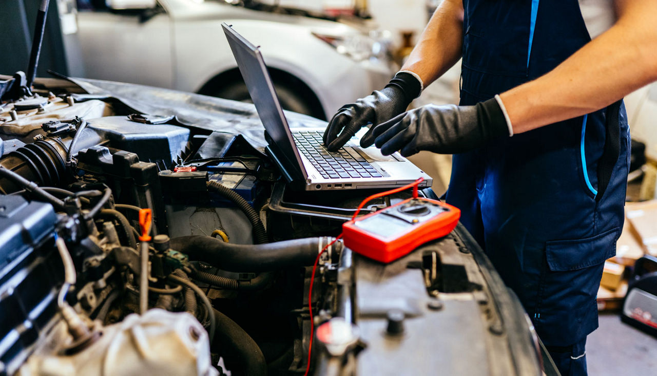 Car electrician using computer in auto repair shop.